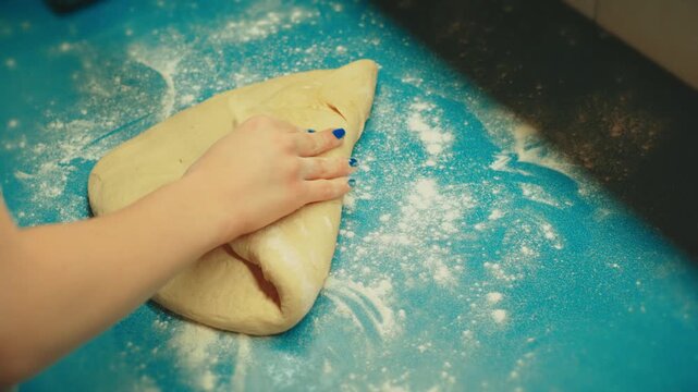 Close up shot of teenage hands using a wooden rolling pin to flatten raw yeast dough on a blue counter. Authentic home baking process for sweet pastry and dessert.