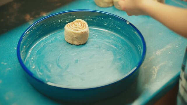 Close up of teenager placing freshly cut raw cinnamon rolls into a greased baking pan. Preparing sweet buns for the oven in a home kitchen setting.