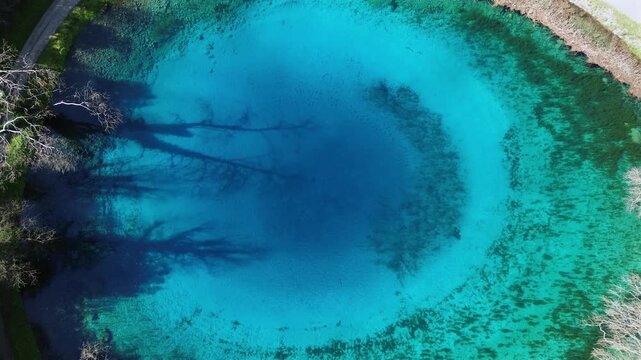 Cinematic drone ascending shot revealing the stunning "Blue Eye" natural spring of Louros. High-angle view of the vibrant turquoise circular lake and crystal clear water. Ideal for nature intros.