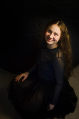 Fototapeta premium A girl crouched on the floor on a black background, dressed in black