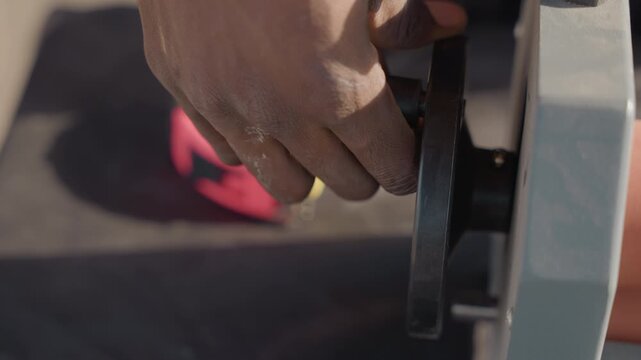 Closeup black hand turning wheel, black carpenter tightens clamp, tape measure nearby, bench shadow, focused grip, tool adjustment, measuring setup, workshop detail, handson trade