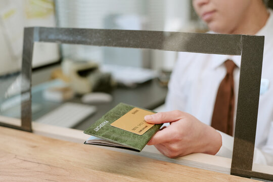 Woman handing bank card and passport through service window at branch counter, focus on hands and documents, customer service representative assisting client transaction