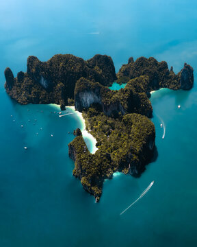 Aerial view of Ko Hong island featuring limestone cliffs, lush greenery, and white sand beaches surrounded by turquoise water with boats in Mueang Krabi District, Krabi, Thailand.