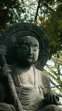 Close-up of Serene Jizo Stone Buddha Statue Framed by Leaves at Japanese Temple, Vertical
