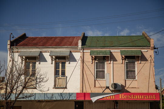 Two adjacent upstairs buildings with contrasting roof colours and awnings under a blue sky