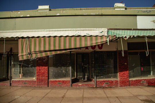 Dilapidated storefront with a torn awning and broken windows on a sunny day