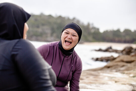 Hmong-American woman laughing openly with her friend in black burkini at the poolside