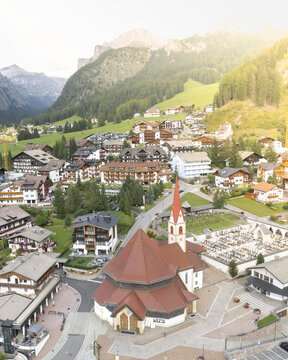 Aerial view of a traditional Alpine village with a red-roofed church and historic chalets nestled in the Dolomites mountains South Tyrol, Trentino-South Tyrol, Italy.
