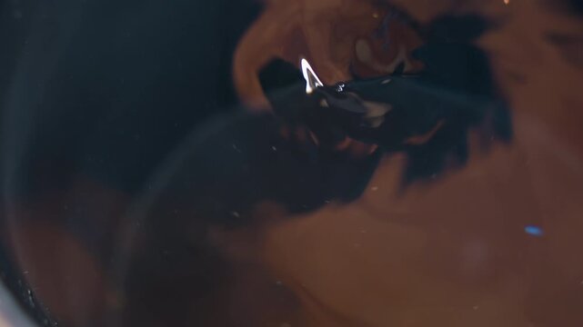 Dark swirling liquid vortex closeup, moody cinematic macro of inkladen coffee droplet plunging into glossy pool forming spiral whirl, subtle bubbles and floating particles, soft reflective highlights,