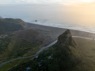Naklejka premium Aerial view of the black sands of Karekare Beach, New Zealand, with the iconic Lion Rock and lush green hills. A popular destination for surfers and nature lovers.
