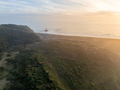 Aerial view of Bethells Beach, New Zealand, showcasing the dramatic coastline and lush green hills. A popular spot for surfers and nature lovers alike.