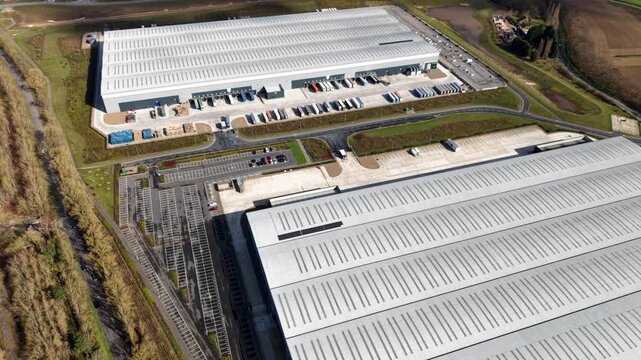 Aerial view of large industrial buildings with vast roofs and parking lots, juxtaposed against the green fields and trees, Doncaster, England, United Kingdom.