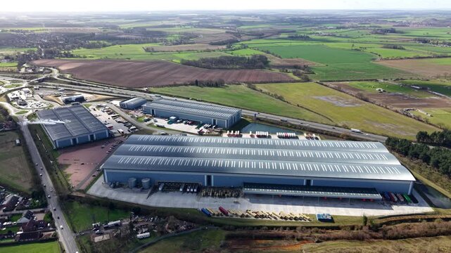 Aerial view of silver industrial buildings surrounded by green fields and roads under a blue sky with clouds, Doncaster, England, United Kingdom.
