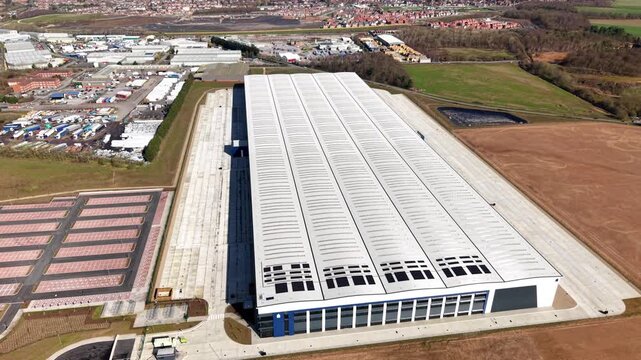 Aerial view of a vast, modern building with a long, light-colored roof contrasting against the surrounding fields and infrastructure, Doncaster, England, United Kingdom.