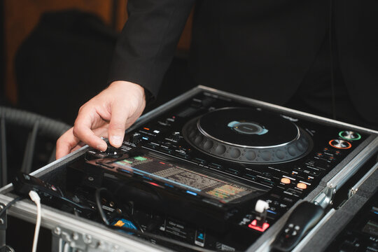 Close up of man artist DJ mixing and scratching music mixer controller. Attractive male musician DJ having fun mixing music on console touching buttons and playing electronic music at neon party