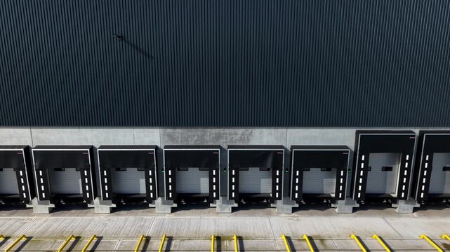 Aerial view of a dark metal warehouse with loading docks displaying a strong contrast between the dark building and the light-colored ground, Doncaster, England, United Kingdom.
