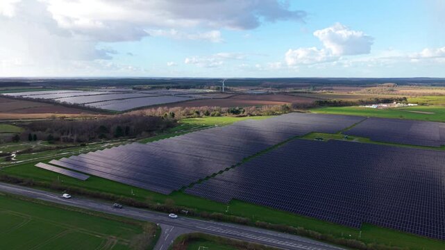Aerial view of expansive solar panel arrays reflecting the sky's hues, juxtaposed against lush green fields, Kirklington Road, Goldbeck Solar Crifton South, United Kingdom.