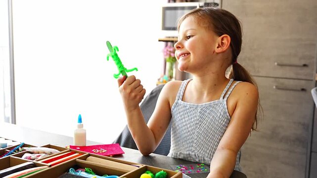 Happy little girl holding handmade craft toy made from wooden stick and pipe cleaners at table. Kids creativity imagination development and learning through play concept.