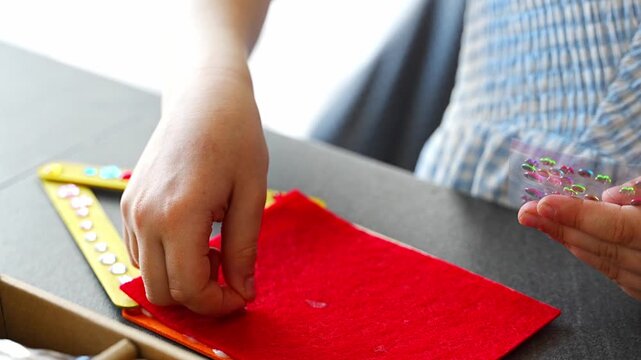 Close up view of hands of little girl decorating handmade craft with colorful self adhesive rhinestones at table. Kids creativity fine motor skills development and learning through play concept.