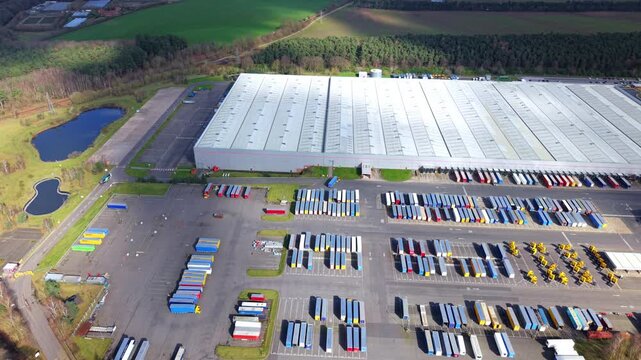 Aerial view of a vast depot, trailers meticulously aligned, contrasting against the backdrop of serene blue ponds and lush green trees, Worksop, England, United Kingdom.