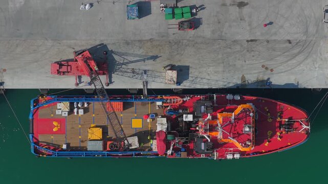 Aerial view of a vibrant red and blue ship moored to a concrete pier, creating a striking contrast with the emerald green water, Ortona, Abruzzo, Italy.