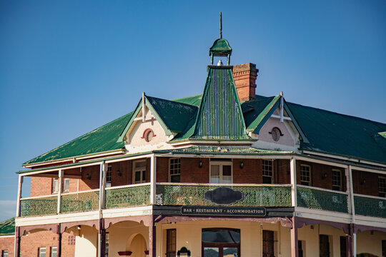 Historic brick building with green corrugated iron roof and ornate balcony under blue sky