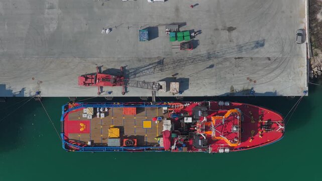 Aerial view of a vibrant red and blue ship docked at the concrete pier, contrasting with the turquoise water, Ortona, Abruzzo, Italy.