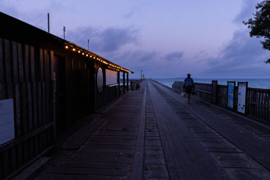 pre-dawn jetty with festoon lights and someone walking out to fish