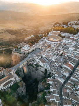 Aerial view of the Puente Nuevo bridge spanning the El Tajo gorge and the historic bullring under golden sunset light in Ronda, Andalusia, Spain.