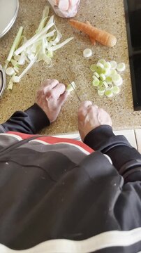 Cortando puerro con cuchillo en trozos y l&aacute;minas con ingredientes en encimera de cocina dom&eacute;stica