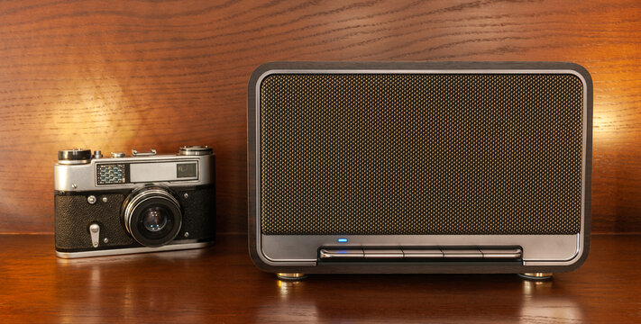A wireless Bluetooth speaker in a retro style and a vintage camera with warm lighting on a wooden shelf