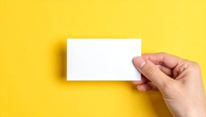Obraz premium Hand holding a blank white card on a vibrant yellow background.