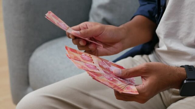 Close-up view of a young man hand counting Indonesia banknotes rupiah money cash
