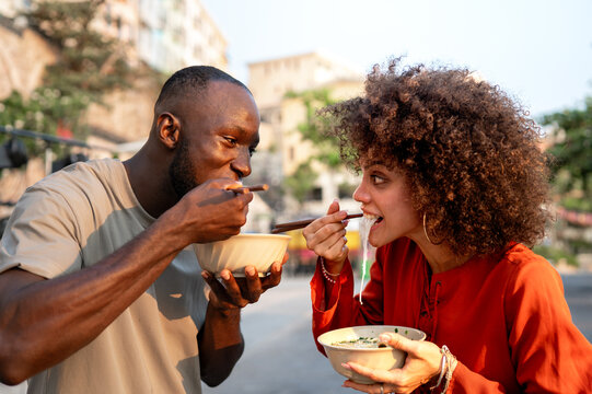 Happy black couple traveling and enjoying exotic street food with chopsticks, having fun