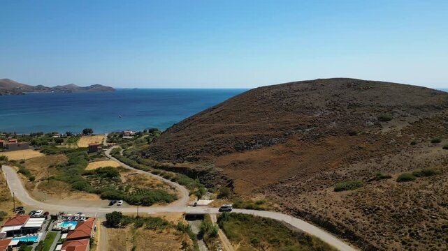 Aerial view of a white camper van traveling along a winding dirt road through the rugged, golden landscape of Limnos Island, Greece, highlighting the freedom of off-grid exploration.