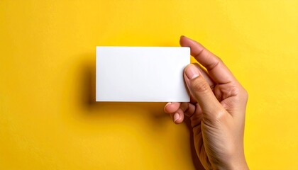 Obraz premium Hand holding blank white business card on vibrant yellow background for branding.