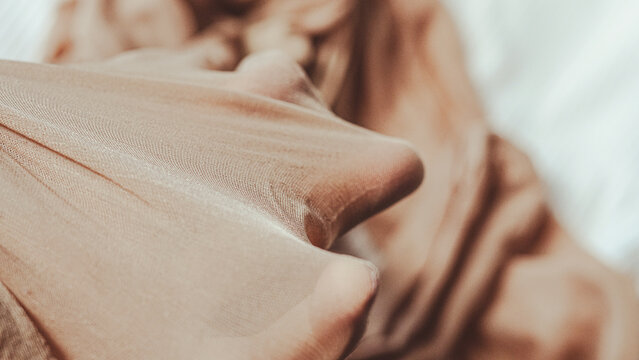 Close-up of sheer fabric draped over hand with soft background texture