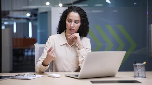 Businesswoman suffering from wrist pain while using computer mouse working on laptop at workplace in modern business office. Sad female employee massages a joint, does an exercise with her hand