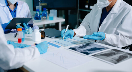 Fototapeta premium Medical team having a meeting with doctors in white lab coats and surgical scrubs seated at a table discussing a patients working online using computers