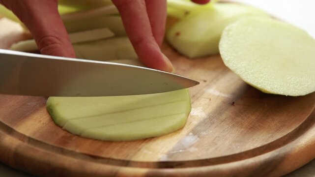 Woman hands slicing fresh green apple into sticks on wooden cutting board, healthy snack preparation