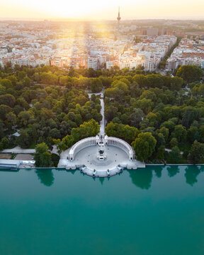 Aerial view of the Monument to Alfonso XII and the Retiro Pond surrounded by lush green trees and the city skyline at sunset in Madrid, Community of Madrid, Spain.