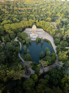 Aerial view of the Palacio de Cristal and its pond surrounded by lush green trees in Retiro Park Madrid, Community of Madrid, Spain.