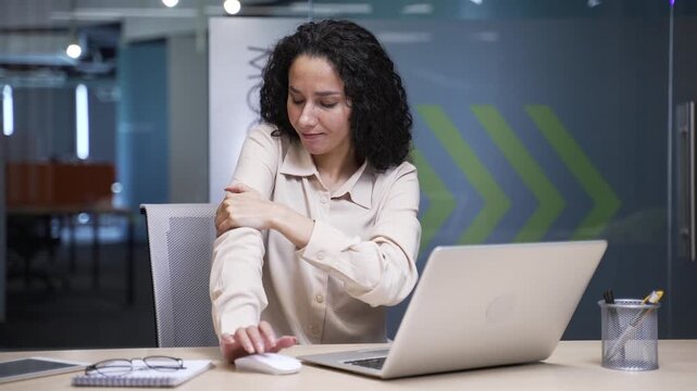 Businesswoman suffering from elbow pain while sitting at a desk at a workplace in a business office. Upset female employee is massaging a joint. The woman has a joint injury or ligament sprain
