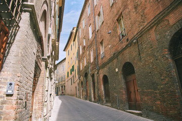 Fototapeta premium Narrow street in Siena Italy with old brick buildings and historic architecture, quiet European town scene under blue sky, travel destination with medieval charm and peaceful urban view