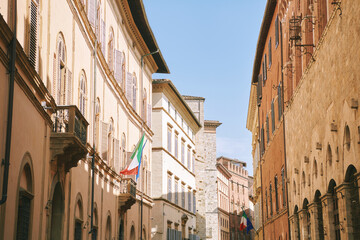 Fototapeta premium Historic street in Siena Italy with old buildings and Italian flags, warm sunlight on stone and brick facades, classic European architecture, travel destination in charming town
