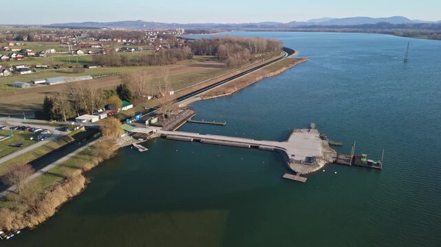 Ptujsko Jezero near Ptuj, Slovenia, features a tranquil lake bordered by marina docks, jetties, and farmland, with the town and surrounding countryside visible in this daytime aerial drone panorama.