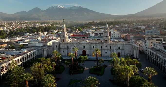 Panorama of Basilica Cathedral of Arequipa over Plaza with palm trees. Volcanoes on horizon.