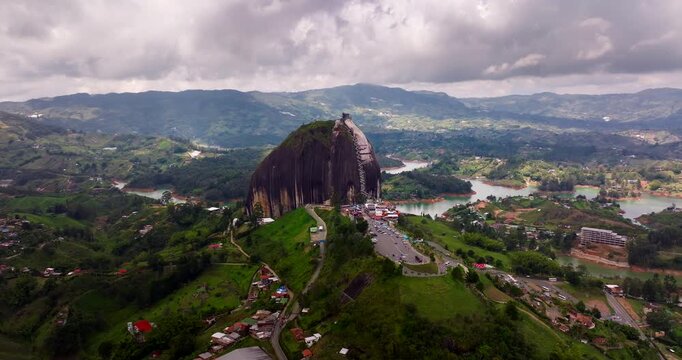 Cinematic Aerial view of La Piedra del Pe&ntilde;ol above the Guatap&eacute; reservoir in Antioquia, Colombia, showing the iconic monolith surrounded by green hills and winding waters