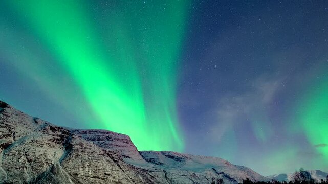 Night sky over snowy mountain illuminated by Northern Lights, Aurora Phenomenon. Skibotn, Norway