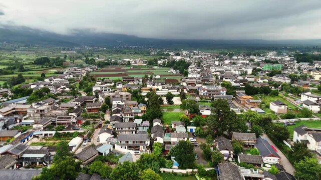 High angle aerial shot of Baisha ancient town near Lijiang, featuring traditional architecture and Fuguo Monastery under a dramatic cloudy sky. Perfect for travel and cultural documentaries.